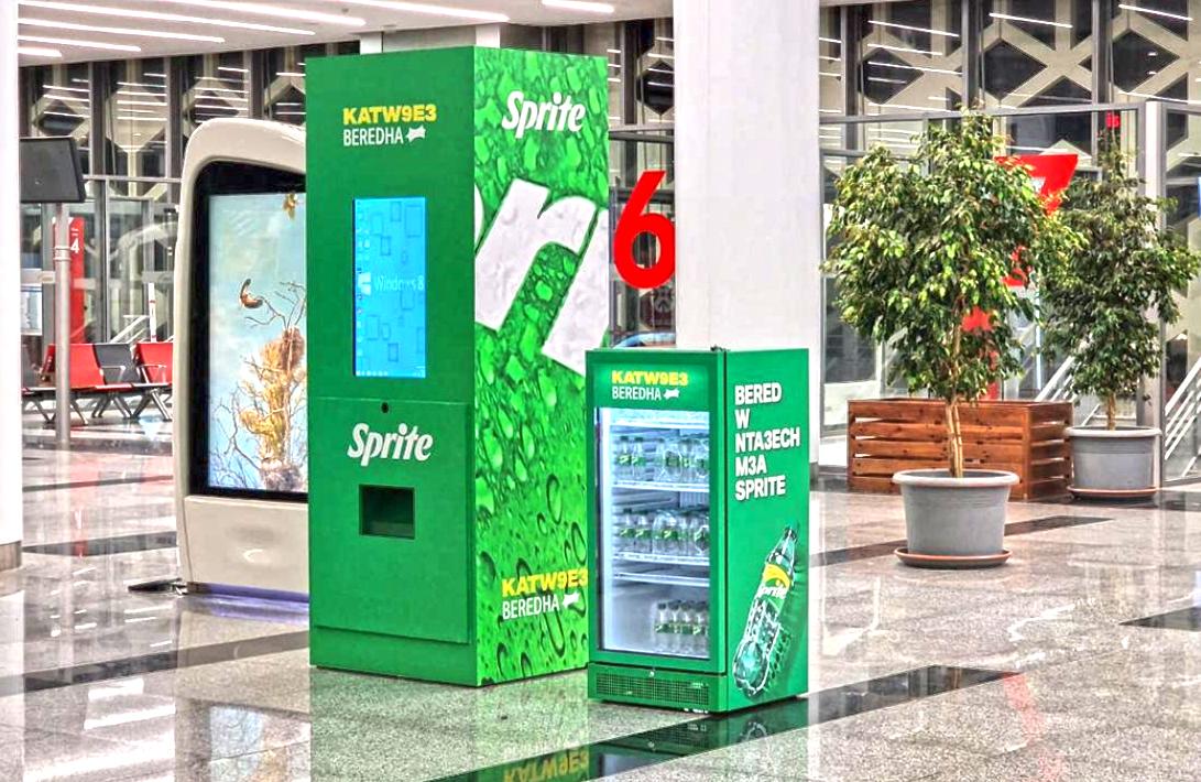 Borne de jeu Sprite à écran tactile et réfrigérateur, dans un hall vitré.